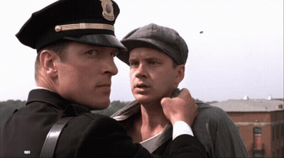A Man In A Police Uniform Holds Another Man 'S Neck GIF