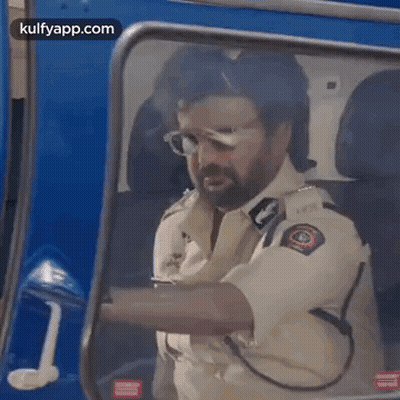 A Man In A Police Uniform Is Driving A Blue Vehicle . GIF