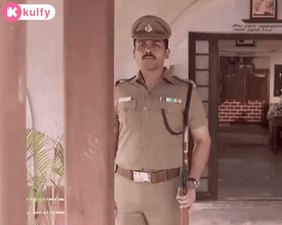 A Man In A Police Uniform Is Holding A Gun In Front Of A Doorway . GIF