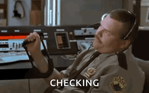 A Man In A Police Uniform Is Sitting At A Desk Holding A Microphone And The Word Checking Is On The Screen . GIF