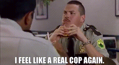 A Man In A Police Uniform Is Sitting At A Table With Another Man And Eating A Hamburger . GIF