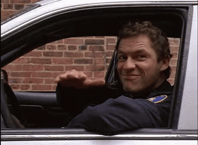 A Man In A Police Uniform Is Sitting In A Car And Waving . GIF