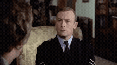 A Man In A Police Uniform Is Sitting In A Chair And Talking To Another Man . GIF