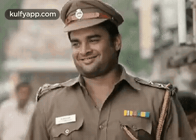 A Man In A Police Uniform Is Smiling While Standing On A Street . GIF