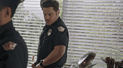 A Man In A Police Uniform Is Standing In Front Of A Window GIF