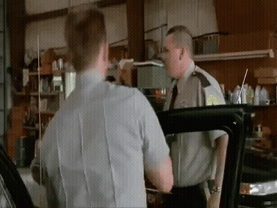 A Man In A Police Uniform Is Talking To Another Man In A Garage While Standing Next To A Car . GIF