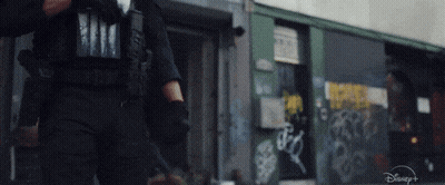 A Man In A Police Uniform Is Walking Down A Street In Front Of A Building With Graffiti On It . GIF