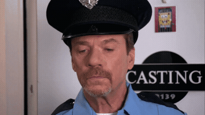 A Man In A Police Uniform Stands In Front Of A Sign That Says Casting GIF