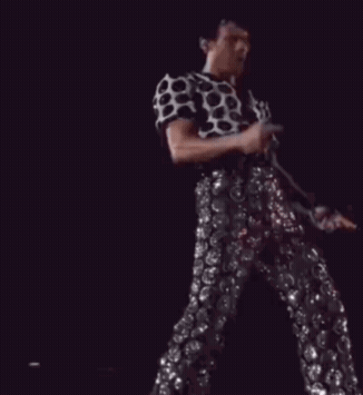 A Man In A Polka Dot Shirt And Sequined Pants Is Dancing On Stage GIF