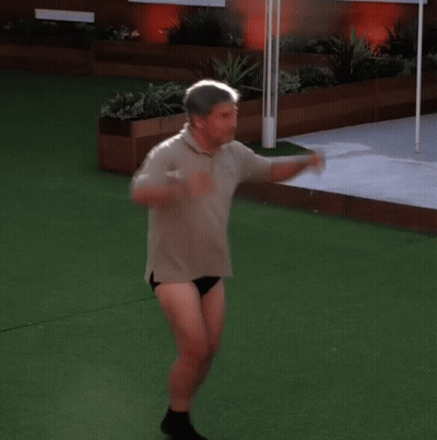 A Man In A Polo Shirt And Black Underwear Is Standing On A Lush Green Field GIF