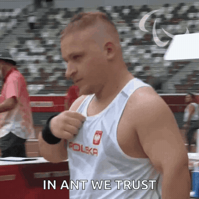 A Man In A Polska Tank Top Is Standing In Front Of A Crowd And Saying In Ant We Trust GIF