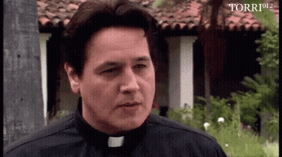A Man In A Priest 'S Collar Is Standing In Front Of A Building With Torri912 Written In The Corner GIF
