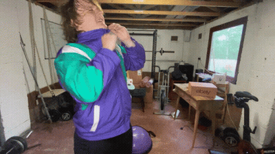 A Man In A Purple And Green Jacket Is Standing In A Garage With A Box That Says Ebay GIF