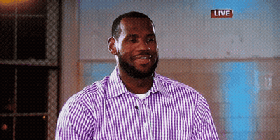 A Man In A Purple And White Checkered Shirt Is Smiling In Front Of A Live Sign GIF