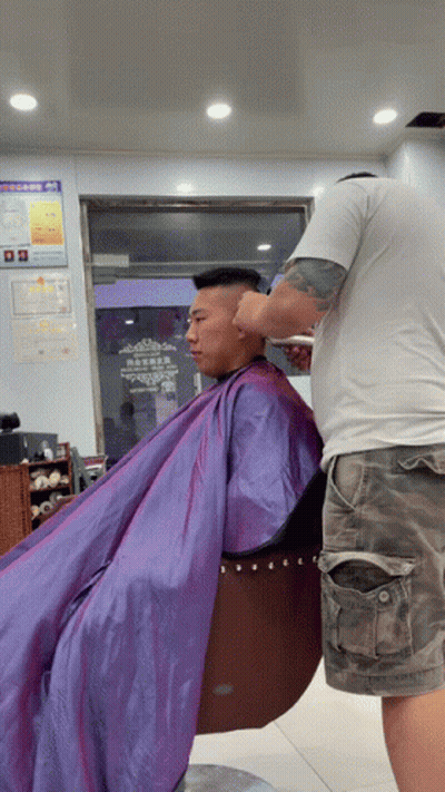 A Man In A Purple Cape Is Getting His Hair Cut By A Man In A White Shirt GIF