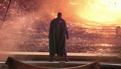 A Man In A Purple Cape Is Standing In Front Of A Fire GIF