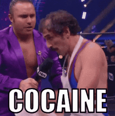 A Man In A Purple Jacket Is Talking Into A Microphone While Another Man Looks On With The Word Cocaine Written In White GIF