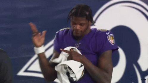 A Man In A Purple Jersey Is Standing In Front Of A Rams Logo . GIF