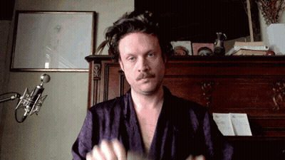 A Man In A Purple Robe Stands In Front Of A Microphone In A Room GIF
