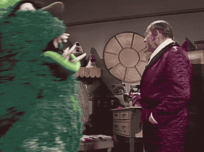 A Man In A Purple Robe Talks To A Green Monster In A Room GIF