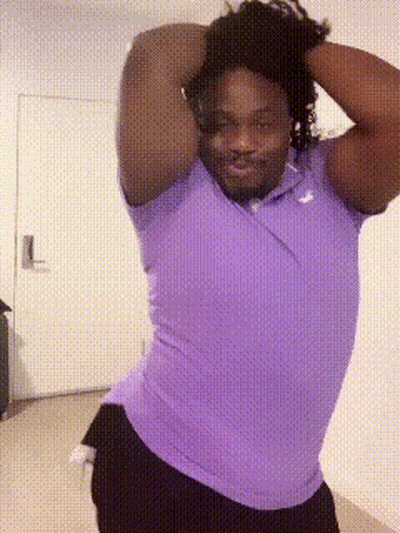 A Man In A Purple Shirt And Black Shorts Is Standing In Front Of A Door GIF