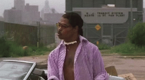 A Man In A Purple Shirt And Glasses Is Standing Next To A Car In A Parking Lot . GIF