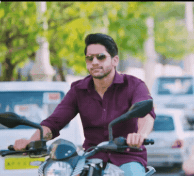 A Man In A Purple Shirt And Sunglasses Is Riding A Motorcycle GIF