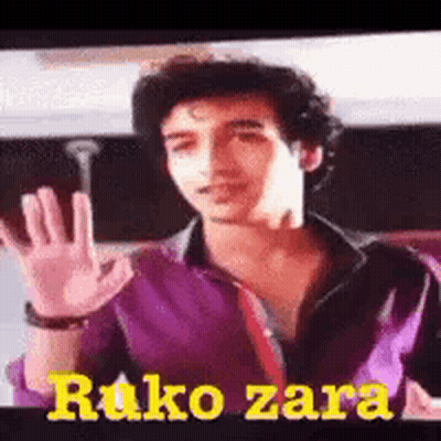 A Man In A Purple Shirt And Tie Is Waving His Hand In Front Of A Screen That Says Ruko Zara GIF