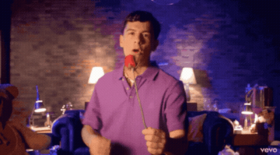A Man In A Purple Shirt Holds A Rose In His Mouth GIF