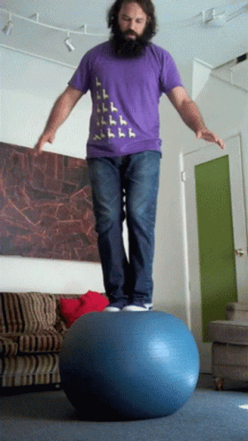 A Man In A Purple Shirt Is Balancing On A Ball GIF