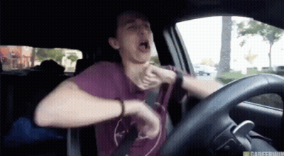 A Man In A Purple Shirt Is Driving A Car And Yawning GIF
