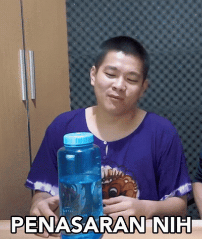 A Man In A Purple Shirt Is Holding A Blue Water Bottle With The Words Penasaran Nih Written On It GIF