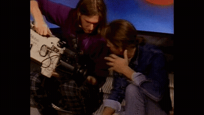 A Man In A Purple Shirt Is Holding A Camera That Says Kodak On It GIF