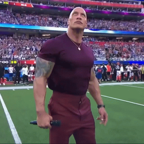 A Man In A Purple Shirt Is Holding A Microphone On A Football Field . GIF