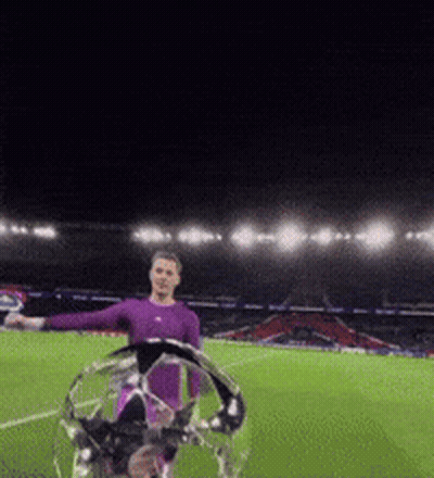 A Man In A Purple Shirt Is Holding A Soccer Ball On A Field At Night GIF