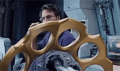 A Man In A Purple Shirt Is Looking At A Large Gold Object In A Room . GIF