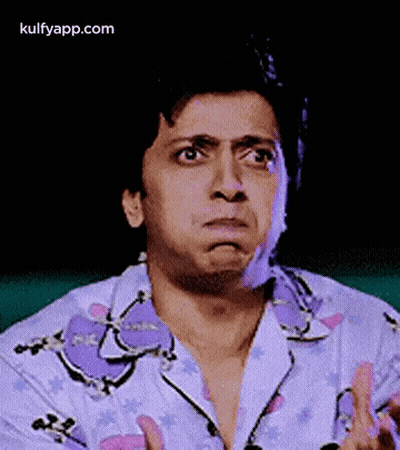 A Man In A Purple Shirt Is Making A Funny Face With His Hands . GIF