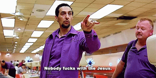 A Man In A Purple Shirt Is Pointing At Another Man In A Bowling Alley While Talking . GIF