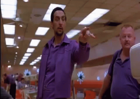 A Man In A Purple Shirt Is Pointing At Someone In A Bowling Alley GIF