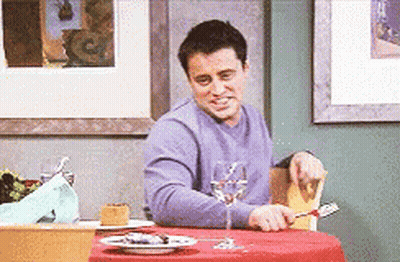 A Man In A Purple Shirt Is Sitting At A Table With A Glass Of Wine . GIF