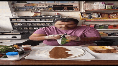 A Man In A Purple Shirt Is Sitting At A Table With A Tortilla On It GIF