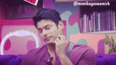 A Man In A Purple Shirt Is Sitting On A Purple Couch In Front Of A Bookshelf GIF