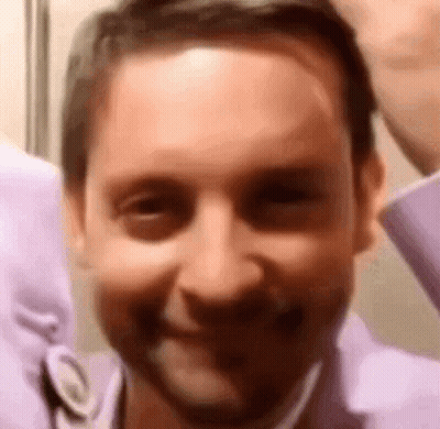A Man In A Purple Shirt Is Smiling For The Camera . GIF