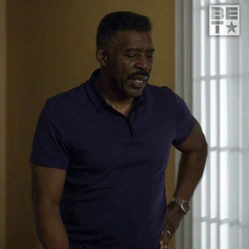 A Man In A Purple Shirt Is Standing In Front Of A Window With A Be I Logo On It GIF