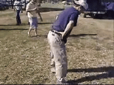 A Man In A Purple Shirt Is Standing In The Grass With His Hands On His Hips . GIF
