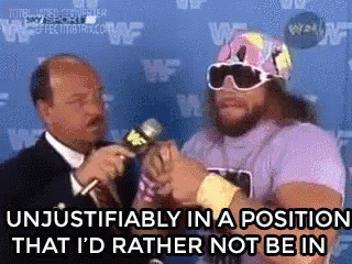 A Man In A Purple Shirt Is Talking Into A Microphone While A Man In A Suit Looks On . GIF