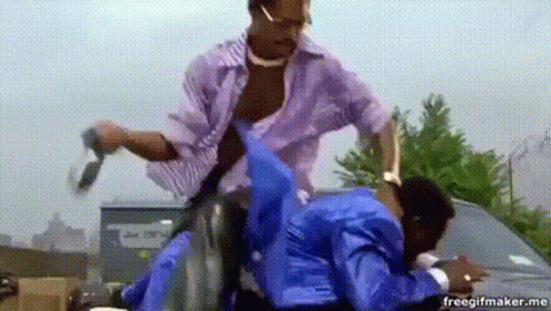 A Man In A Purple Shirt Is Talking On A Cell Phone While Another Man In A Blue Jacket Holds A Gun . GIF