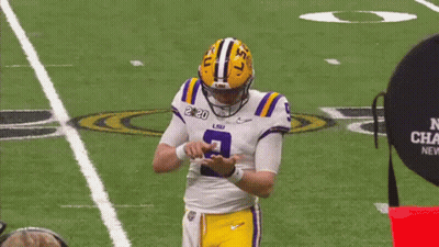 A Man In A Purple Shirt Is Talking To A Football Player In A Lsu Uniform . GIF