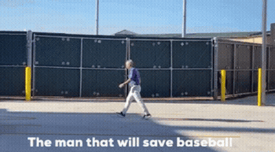 A Man In A Purple Shirt Is Walking Down A Street With The Words " The Man That Will Save Baseball " Written Below Him GIF