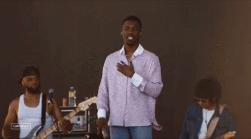 A Man In A Purple Shirt Sings Into A Microphone While Another Man Plays Guitar GIF